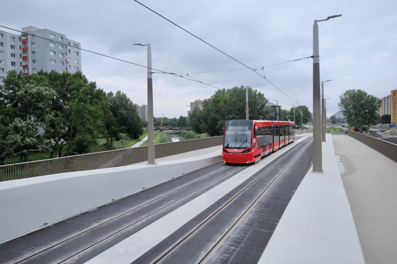Električka na jednom z vybudovaných mostov na predĺženej trati v Petržalke. V pozadí stromy a bytový dom.